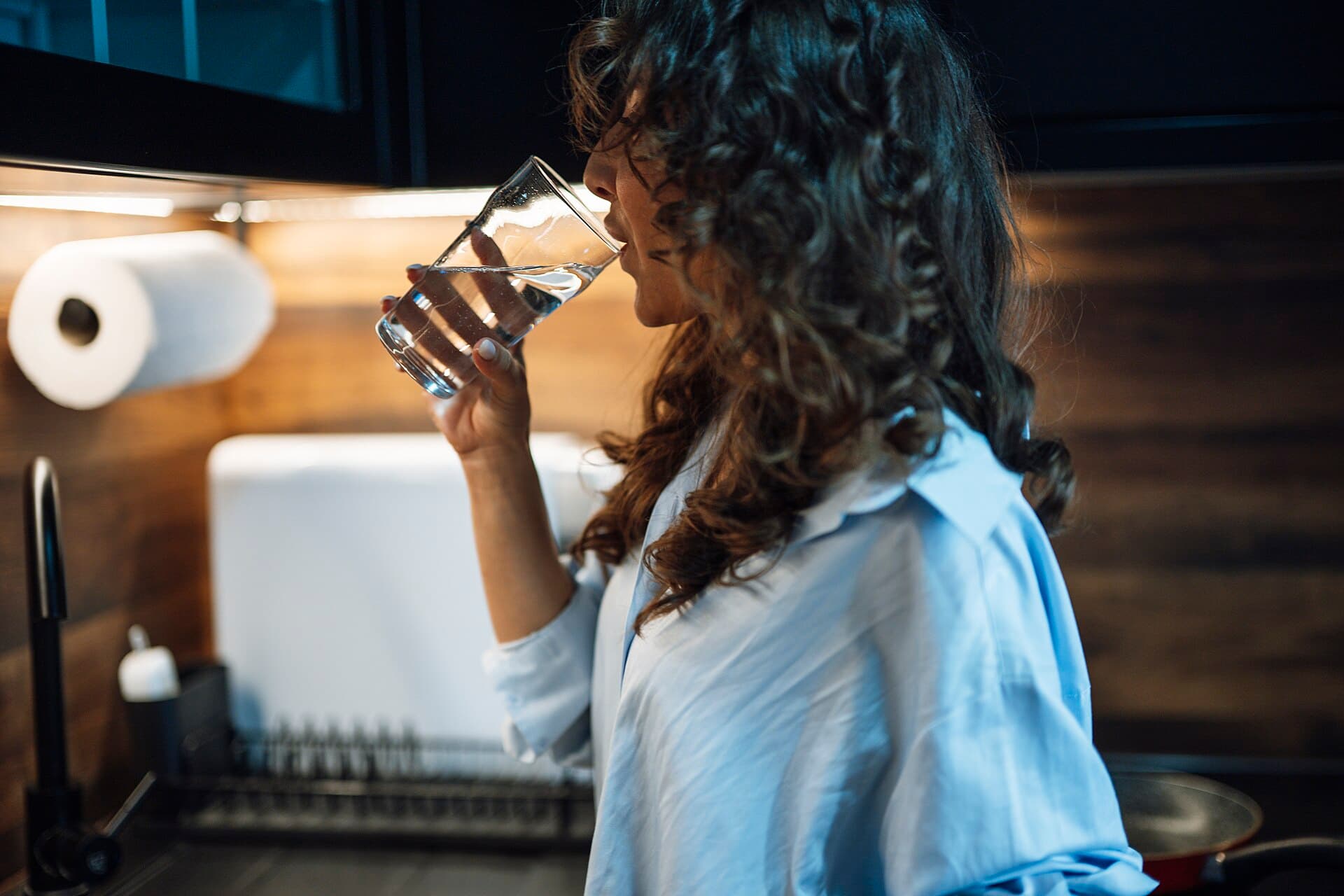 A woman drinks water from a glass in a modern kitchen